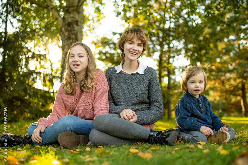Two big sisters and their toddler brother having fun outdoors. Two young girls with a toddler boy on autumn day. Children with large age gap. Big age difference between siblings. Two big sisters and their toddler brother having fun outdoors. Two young girls with a toddler boy on autumn day. Children with large age gap. Big age difference between siblings.