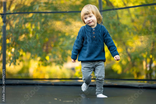 Cute toddler boy jumping on a trampoline in a backyard on warm and sunny summer day. Sports and exercises for children. Summer outdoor activities. © MNStudio