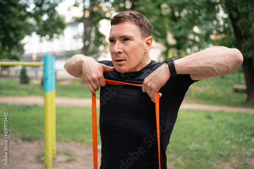 Middle age man doing strength exercises with resistance bands outdoors in park 