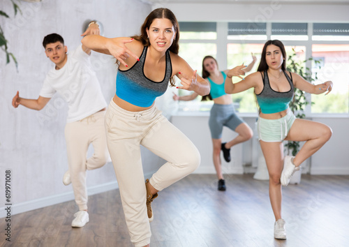 Positive female teenager dances groove in choreographic school, group of young people in sportswear trains together with their classmates in gym before competitions, battle