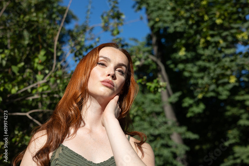 very beautiful freckled white woman with long red hair in a garden of green leaves