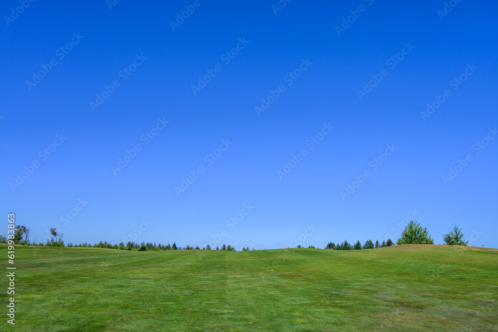 Relaxing day on the golf course, fairway grass running up to clear blue sky, recreation and challenge on a sunny summer day
