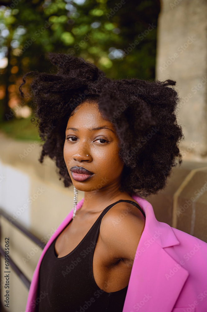 Fashion outdoor street style portrait of Beautiful young African American woman posing outside on urban city landscape summer day wearing pink jacket. Attractive black female, diversity concept Fashion outdoor street style portrait of Beautiful young African American woman posing outside on urban city landscape summer day wearing pink jacket. Attractive black female, diversity concept