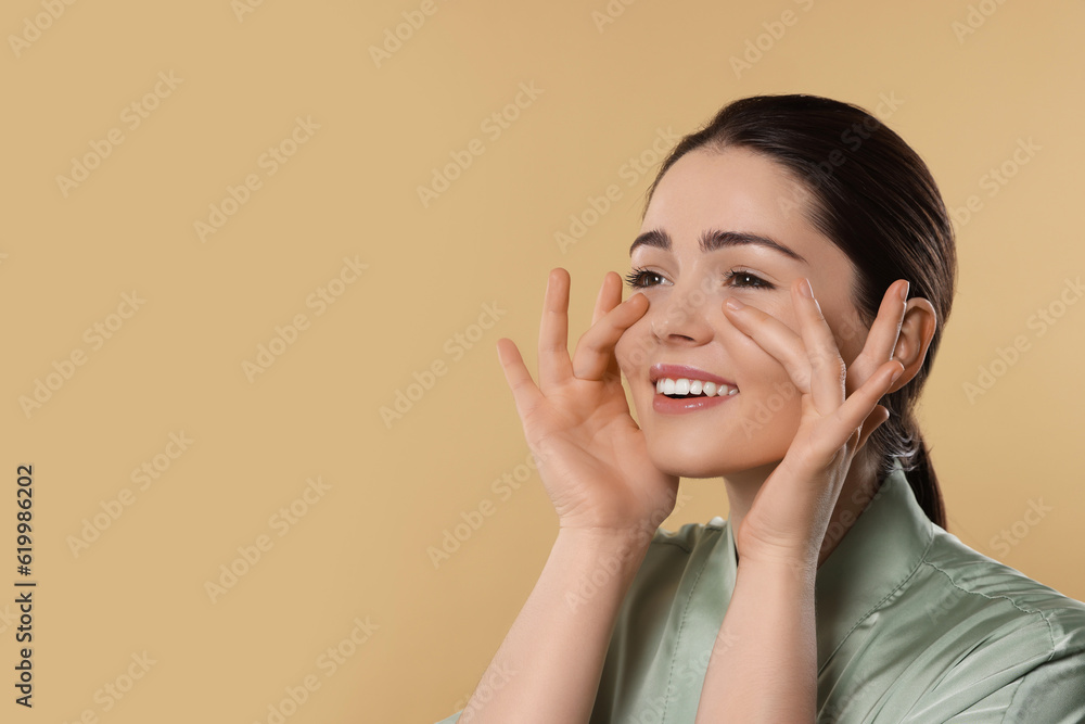 Young woman massaging her face on beige background. Space for text Young woman massaging her face on beige background. Space for text