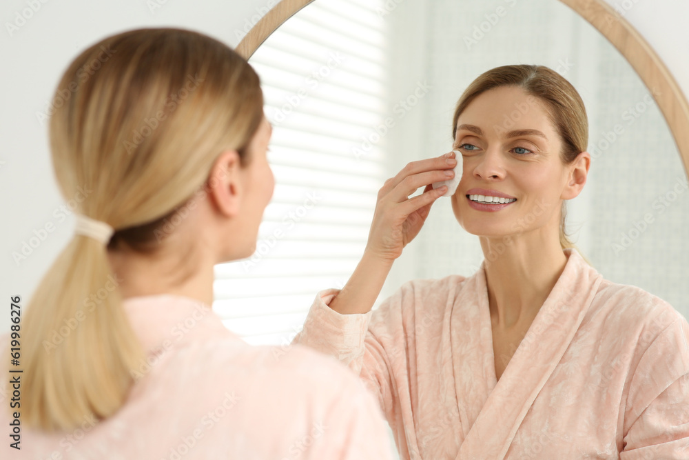 Beautiful woman removing makeup with cotton pad near mirror indoors Beautiful woman removing makeup with cotton pad near mirror indoors