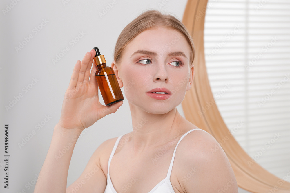 Fototapeta premium Young woman with bottle of essential oil in bathroom