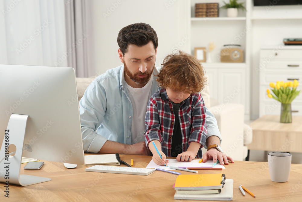 Father spending time with his son at desk. Taking break in remote work at home Father spending time with his son at desk. Taking break in remote work at home
