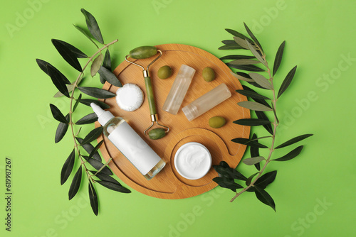 Different cosmetic products, face roller and olives on light green background, flat lay