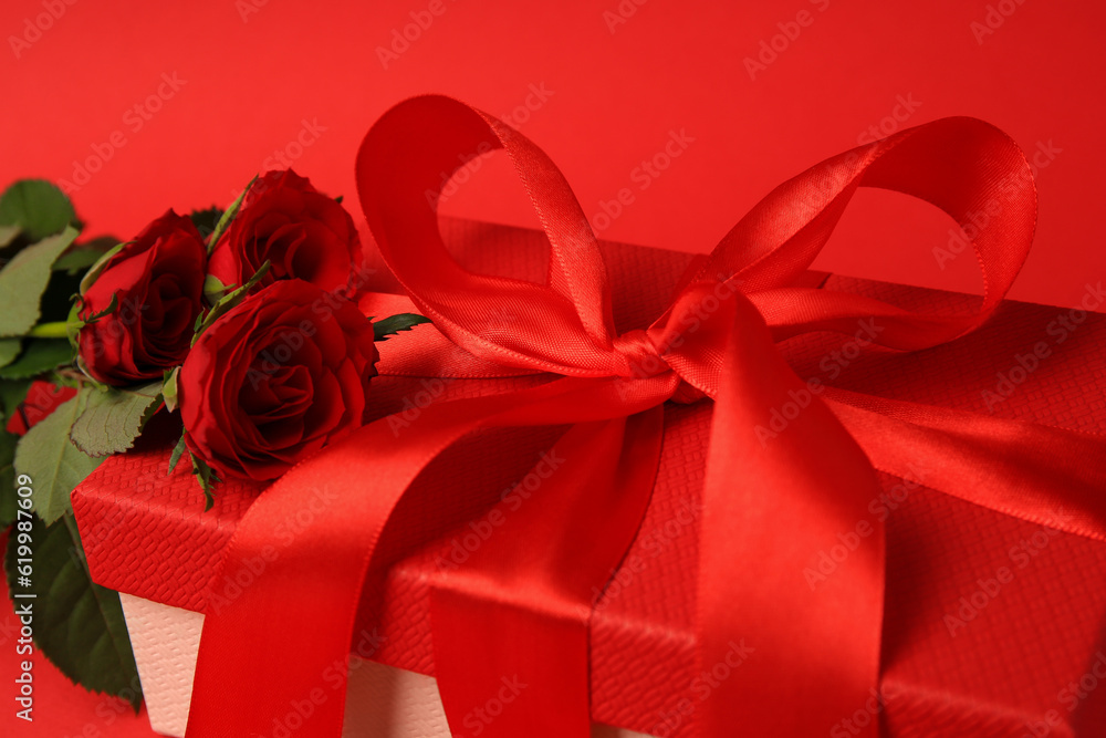 Beautiful gift box with bow and roses on red background, closeup Beautiful gift box with bow and roses on red background, closeup