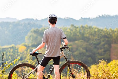 Athlete standing with his mountain bike on top of a hill contemplating the beautiful landscape on a sunny day