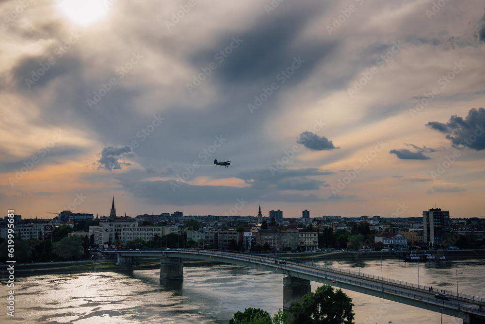 An old biplane flying over the evening city of Novi Sad, Serbia against the background of amazing clouds. Chemical treatment of the territory from mosquitoes and insects