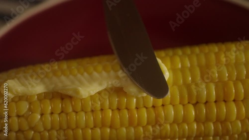 close-up of knife buttering cooked corn on the cob in slow motion