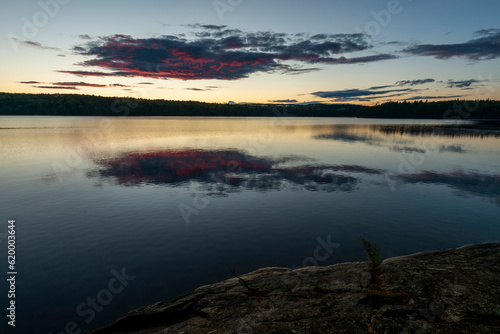 a dark purple and pink clouds getting the final rays of a setting sun reflecting on a calm lake 