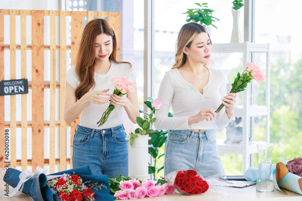 Asian professional successful female florist designer flower shop owner entrepreneur and colleague employee helping decorating pink roses bouquet in white ceramic vase in floral garden store studio