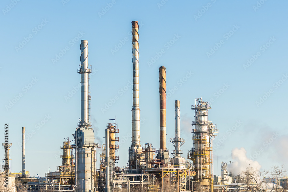 Spiral Topped Spires. Oil refinery in cold blue winter. Tall steam towers and cooling smoke stacks, a facility for receiving and processing oil and fossil fuels