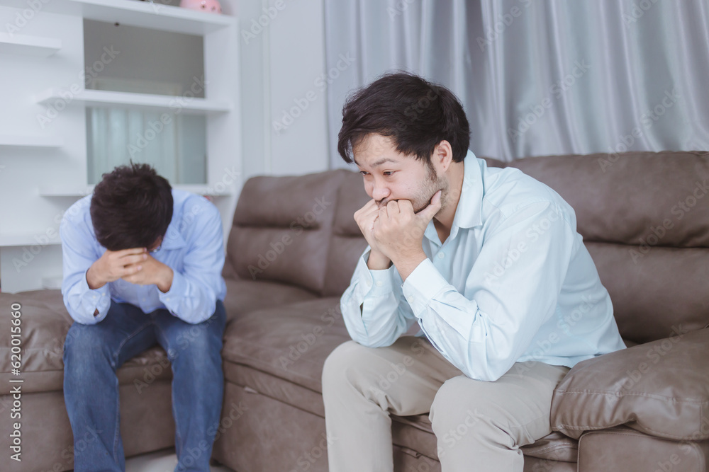 Caucasian gay couple having argument with each other in bedroom. Frustrated gay man sitting on bed with pondering and sad look while another offended guy is sitting behind - Homosexual love concept