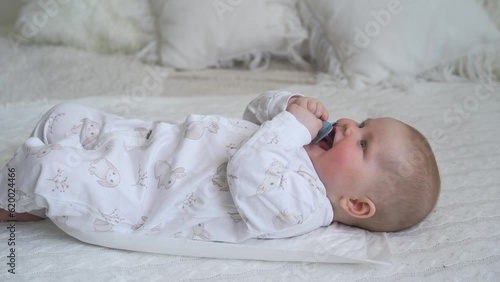 Newborn cheerful littlebaby is chewing and playing in his crib with nipple. Funny smiling looks through the railing of the crib. slow motion. High quality 4k footage photo