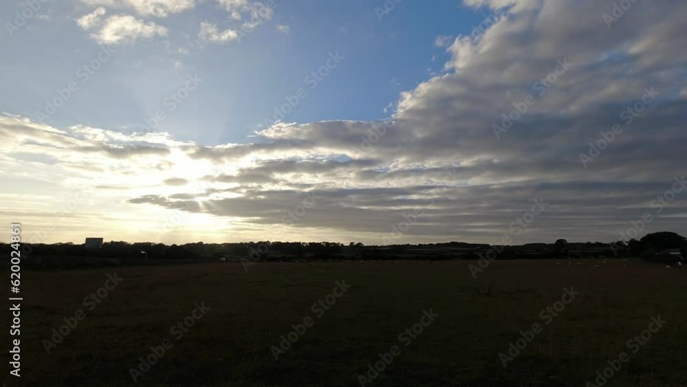 Time lapse sunset clouds changing above Welsh agricultural field with grazing sheep and passing traffic Time lapse sunset clouds changing above Welsh agricultural field with grazing sheep and passing traffic