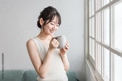 保温マグカップで朝、家でお茶・白湯を飲むリラックスするアジア人女性（温活） 