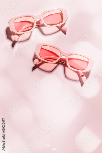 Two pink sunglasses on pink background at sunlight with shadow. Summer fashion eyeglasses with rose tinted glass. Summer romance vacation, rest concept. Minimal style flatlay, top view