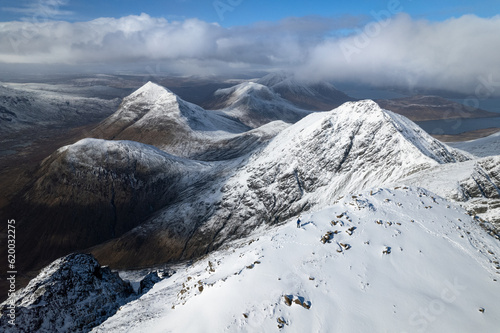 Aerial view of a man standing atop the snow-covered Bla Bheinn mountain, looking at the snow-covered landscape of the Isle of Skye, Scotland. photo