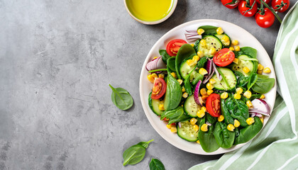 Spring vegan salad with spinach, cherry tomatoes, corn salad, baby spinach, cucumber and red onion. Healthy food concept. Gray stone table. Top view. Copy space