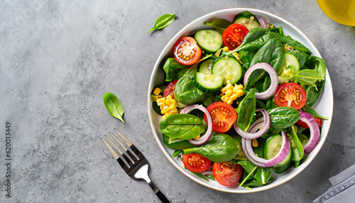 Spring vegan salad with spinach, cherry tomatoes, corn salad, baby spinach, cucumber and red onion. Healthy food concept. Gray stone table. Top view. Copy space