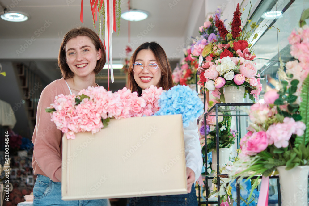 Portrait of two young beautiful female florists with floral bunch delivery, smiling and looking at camera, lovely business entrepreneur, flower shop happy work, brightly colorful flora bouquet store.