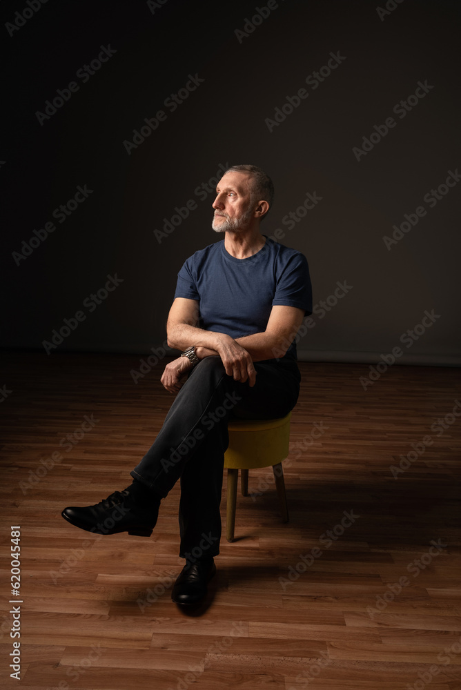 an ordinary adult man with a beard is sitting on a chair in the studio, dark background, selective focus an ordinary adult man with a beard is sitting on a chair in the studio, dark background, selective focus