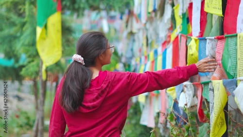 Tourist Indian girl touching Buddhist prayer flags in Himalayan Nyingmapa Gompa, mall road Manali, India. Spiritual person in monastery.  