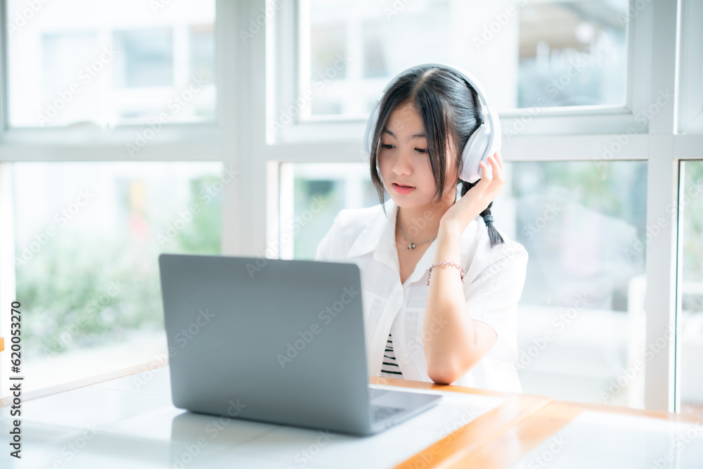 Happy of cute smiles Asian of attractive young Cute girl little wearing headphones and listening music using laptop computer working from at the cafe.Online education, elearning concept. Happy of cute smiles Asian of attractive young Cute girl little wearing headphones and listening music using laptop computer working from at the cafe.Online education, elearning concept.