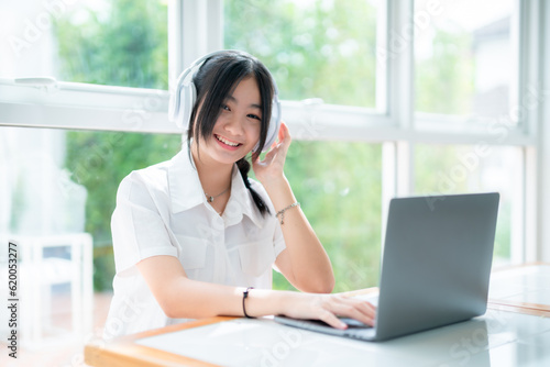 Happy of cute smiles Asian of attractive young Cute girl little wearing headphones and listening music using laptop computer working from at the cafe.Online education, elearning concept.