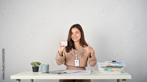 Young cheerful Asian businesswoman holding credit card and smiling to the camera