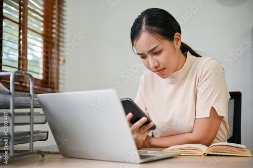Young stressful woman working from home with smartphone and laptop