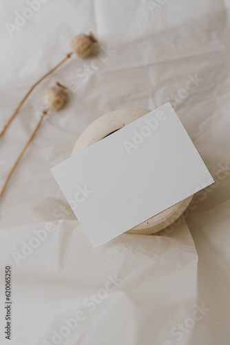 Flat lay blank card sheet, dried poppy stem, clay jar on white crumpled cloth. Top view aesthetic mock up with empty free copy space