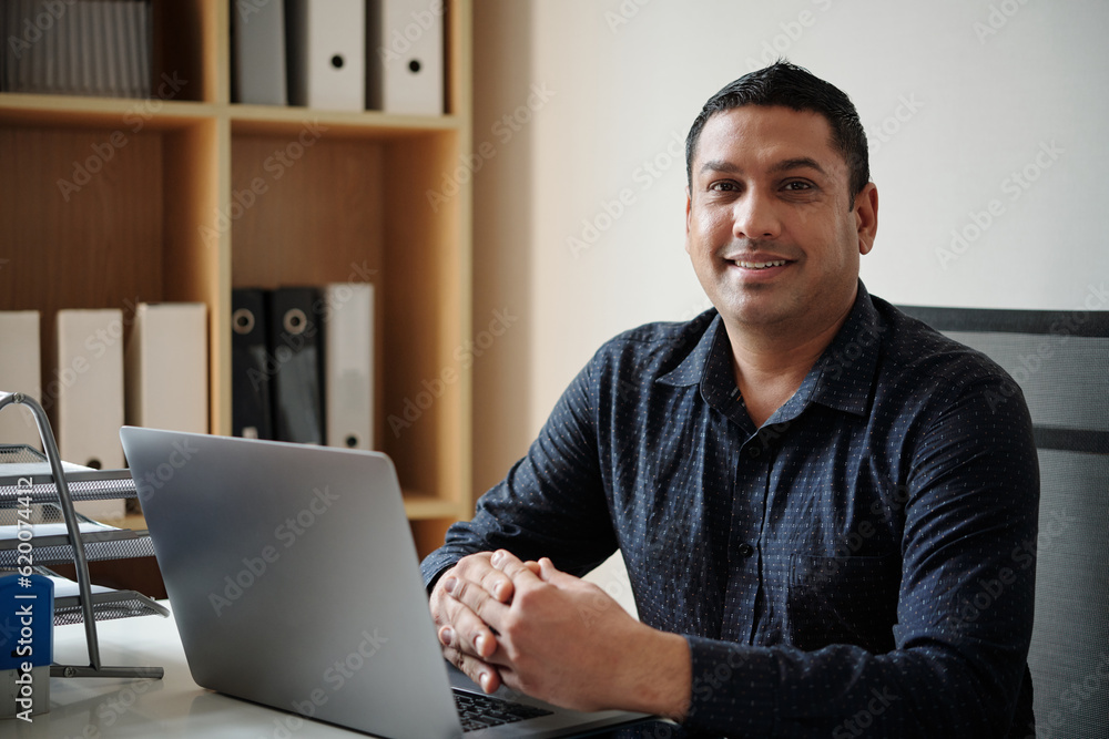Portrait of cheerful entrepreneur working on laptop at office desk Portrait of cheerful entrepreneur working on laptop at office desk