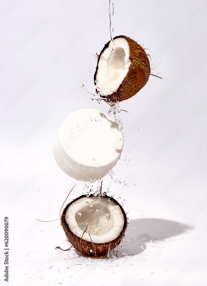Coconut with water splashes and cream jar on white grey background Coconut with water splashes and cream jar on white grey background