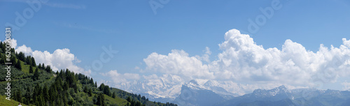 Aerial wide panorama showing Mont Blanc Massive eternal snow tops in atmospheric haze with dramatic clouds rising above seen from Col de Joux Plane