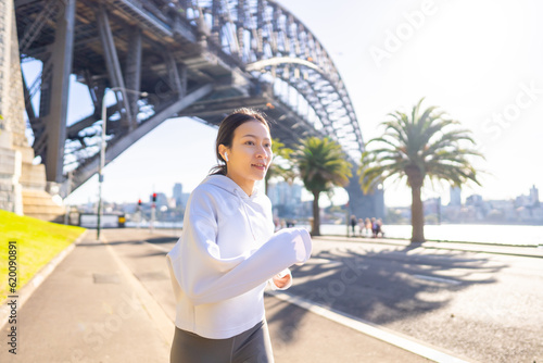 Photography Asian woman in sportswear listening to music from earphones with mobile phone app during jogging exercise at city street in the morning