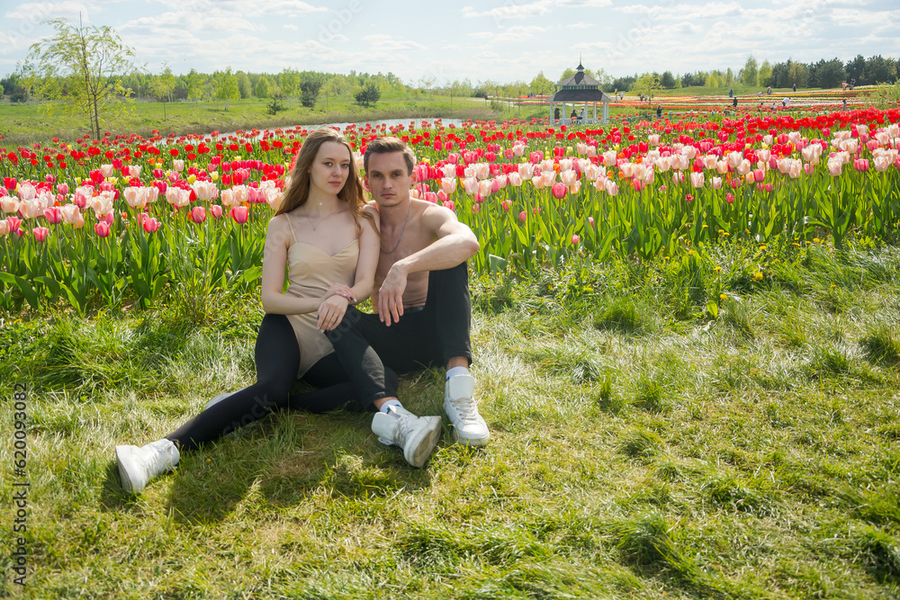 Young beautiful smiling couple sits on the background of a field of colorful tulips.