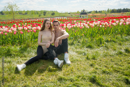 Obraz na płótnie Young beautiful smiling couple sits on the background of a field of colorful tulips. w salonie
