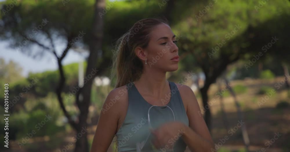 The girl in leggings and a crop top, with a ponytail and headphones in her ears, stops tiredly after her run.