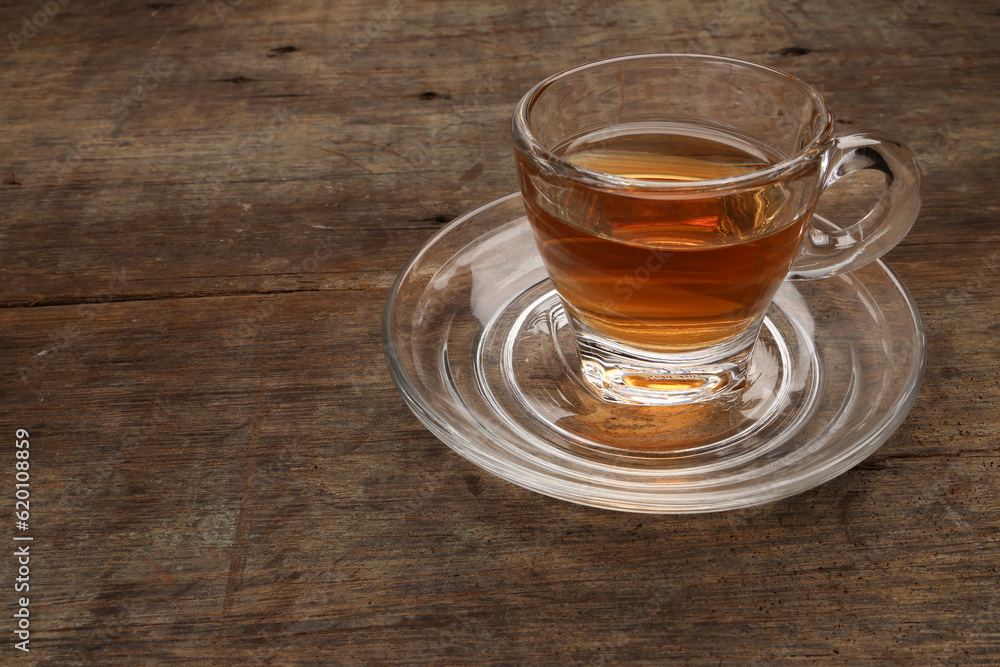 Hot tea in transparent glass cup saucer on rustic wood background Hot tea in transparent glass cup saucer on rustic wood background