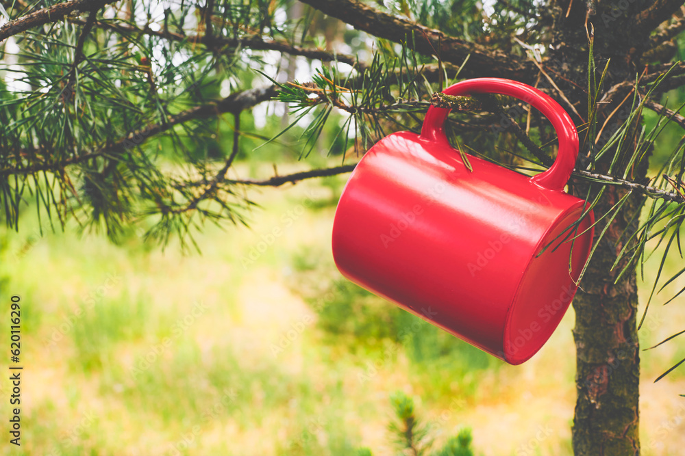 Mug red cup for a drink hanging on a tree in the twilight of a summer day Mug red cup for a drink hanging on a tree in the twilight of a summer day