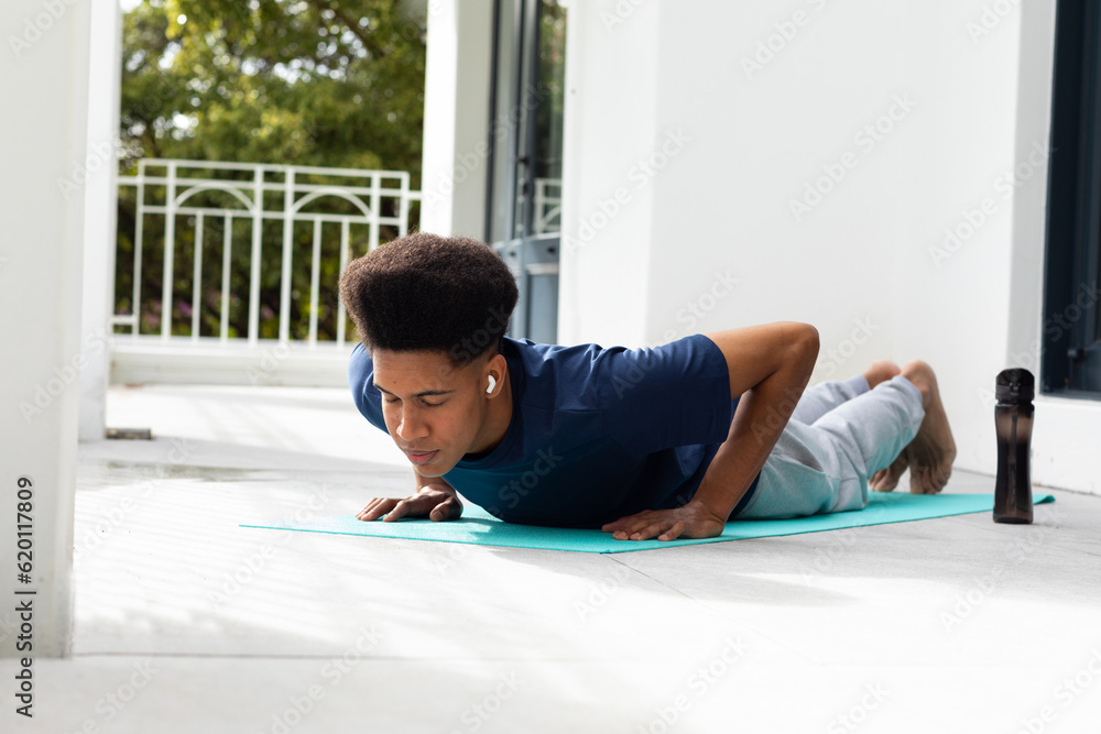 Fototapeta premium Focused biracial man doing yoga lying on sunny balcony