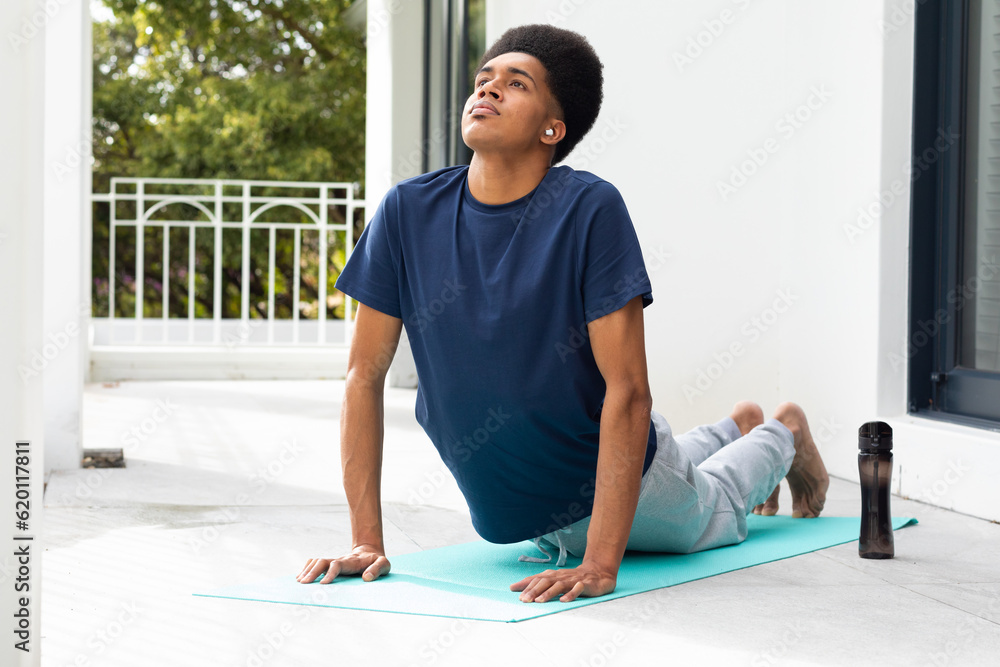 Fototapeta premium Focused biracial man doing yoga lying on sunny balcony