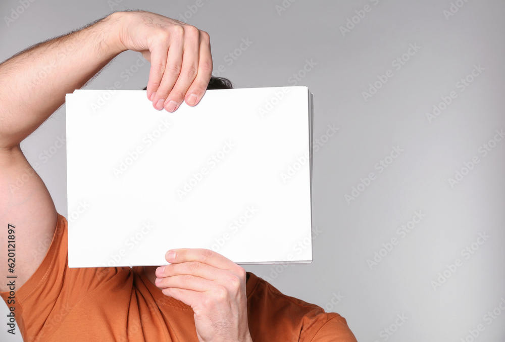 Man covering face with sheet of paper on light grey background. Mockup for design Man covering face with sheet of paper on light grey background. Mockup for design