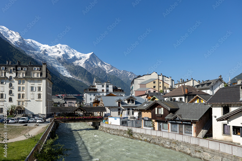River running through French village at the feet of the Mont Blanc Massive mountain range with eternal snow tops in the background during summer. Tourist destination