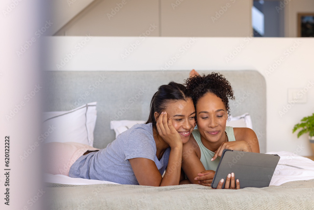 Happy biracial lesbian couple using tablet on bed in bedroom Happy biracial lesbian couple using tablet on bed in bedroom