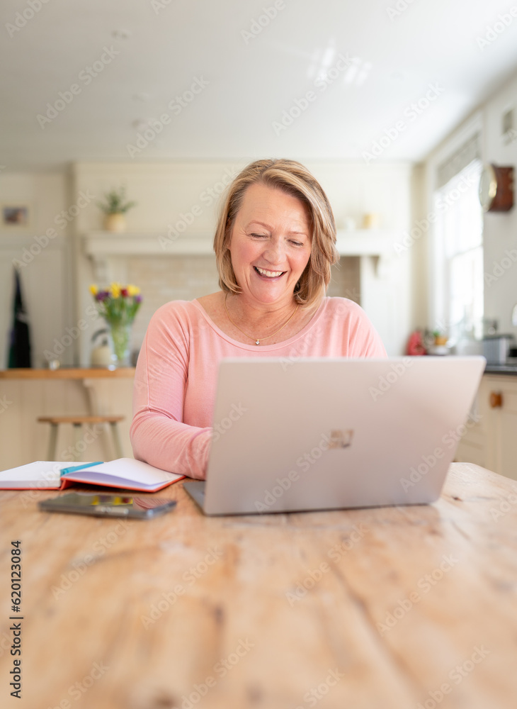 Smiling Woman using laptop working from home in kitchen Smiling Woman using laptop working from home in kitchen